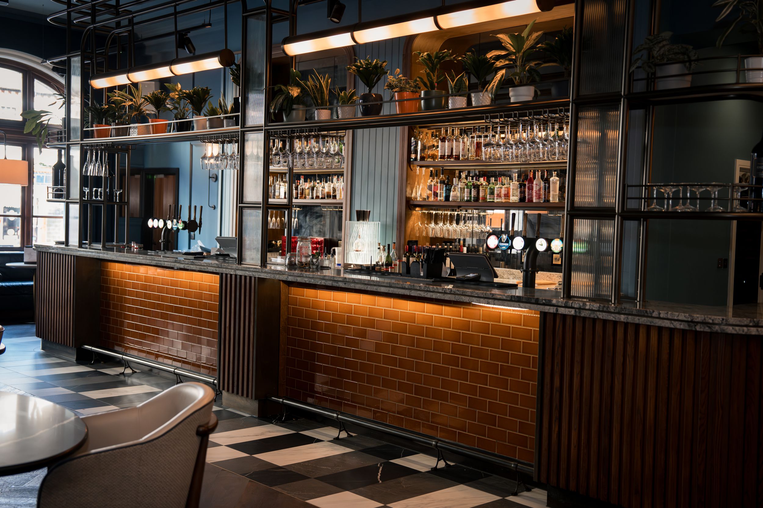 Elegant bar interior with wooden counter, checkered floor, and shelves lined with liquor bottles in a stylish restaurant.
