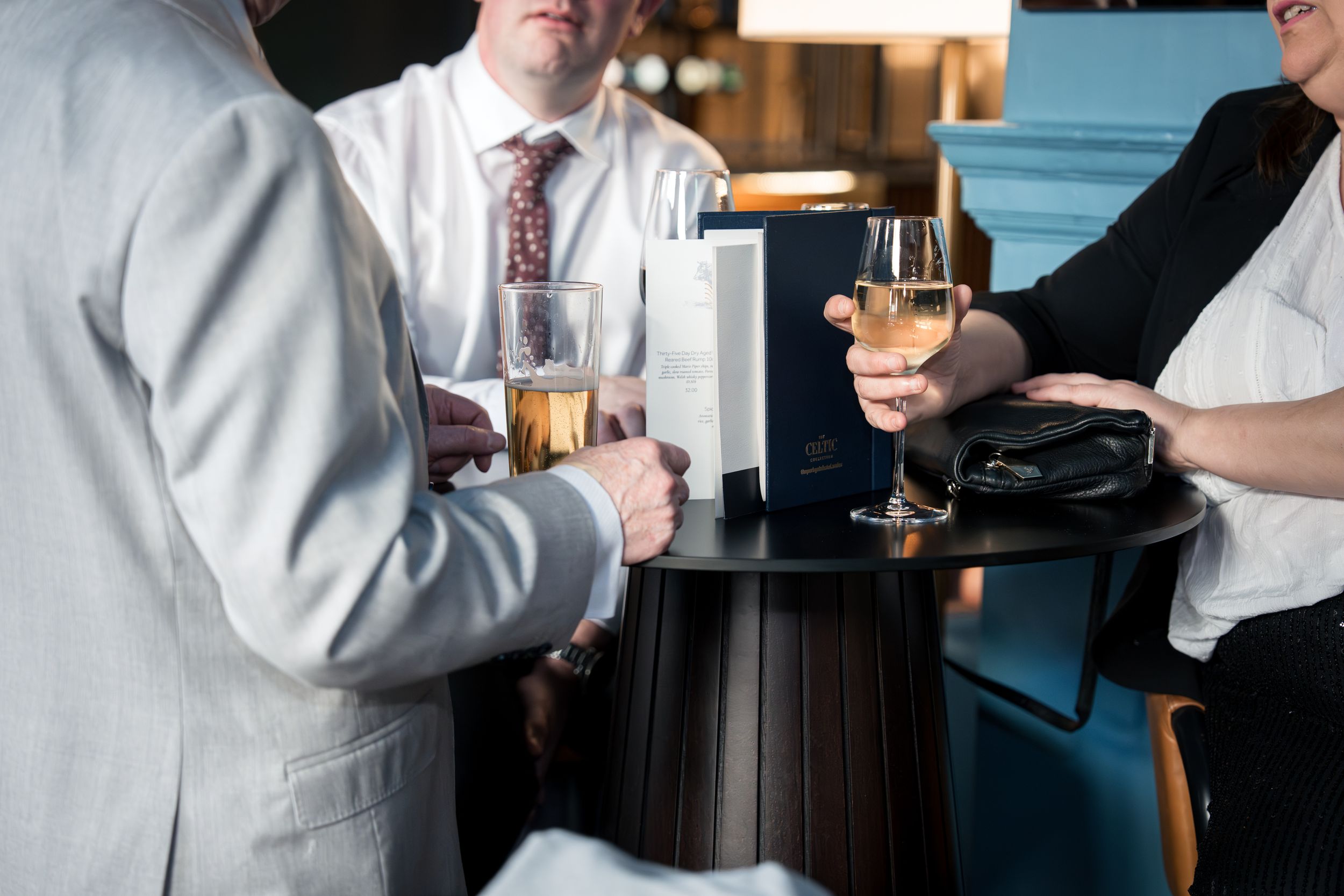 Business professionals networking at a cocktail reception, holding champagne glasses around a small round table.