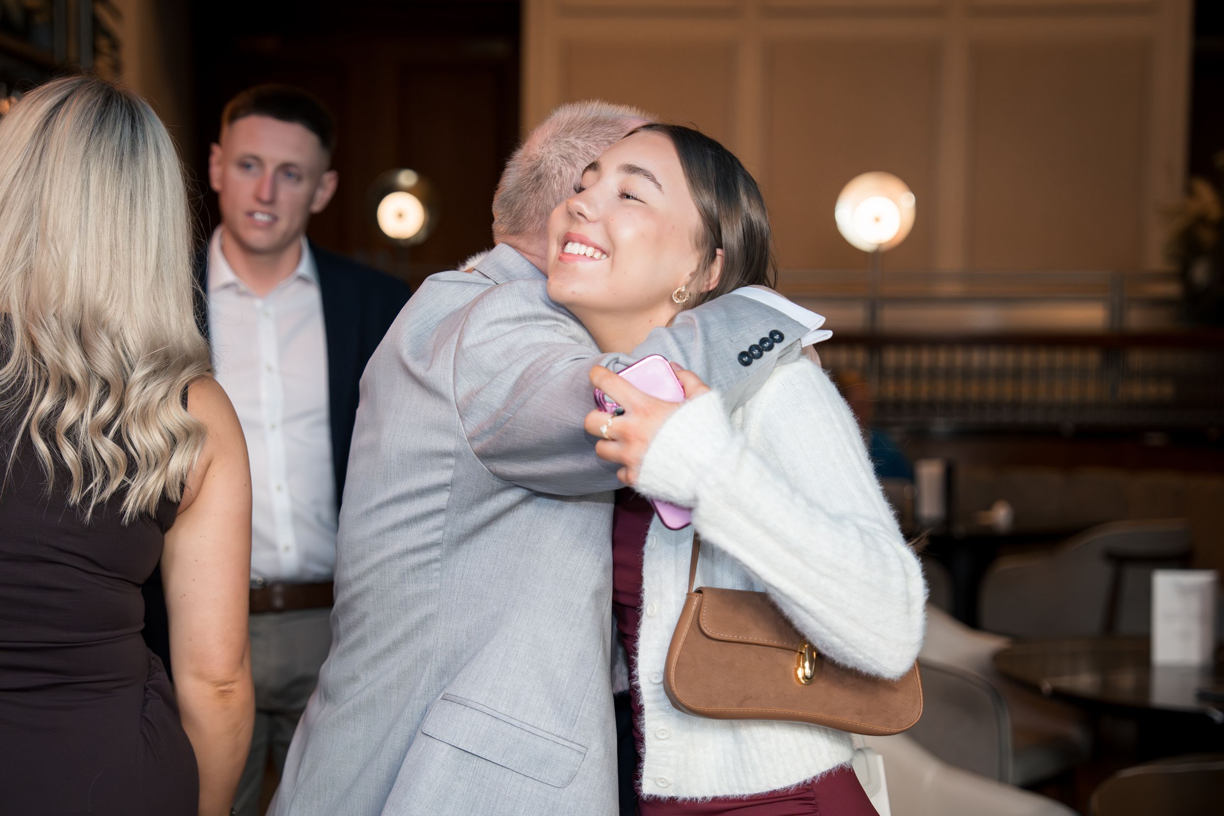 Two women share a warm hug at a wedding reception in a stylish indoor venue.