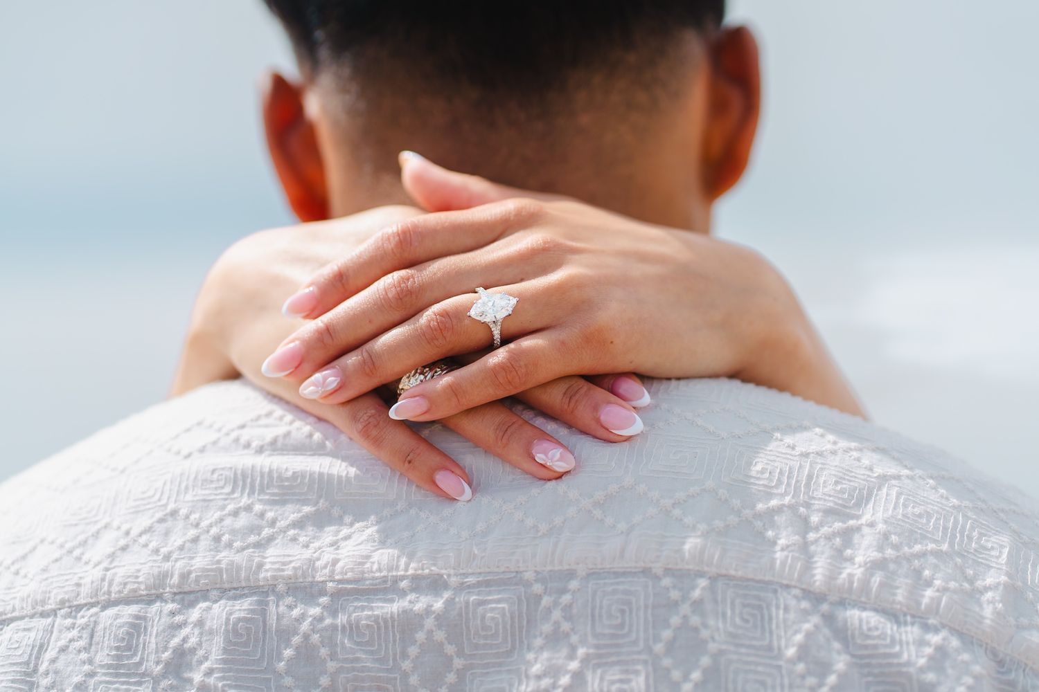 Close-up of a woman's hand with a diamond engagement ring resting on a man's shoulder. Carlsbad, CA