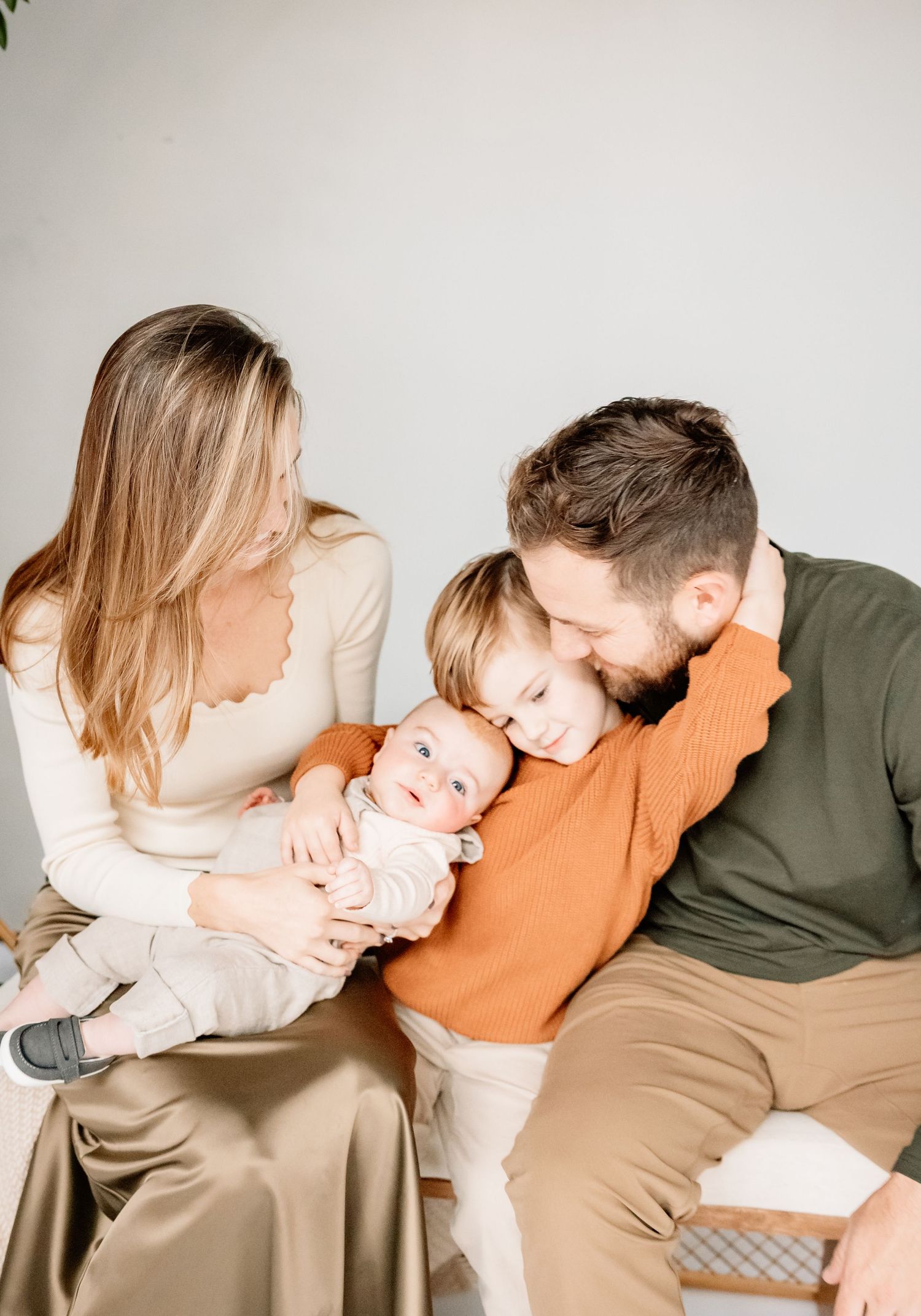 A young family with a newborn baby and toddler sharing a tender moment, dressed in warm neutral tones.