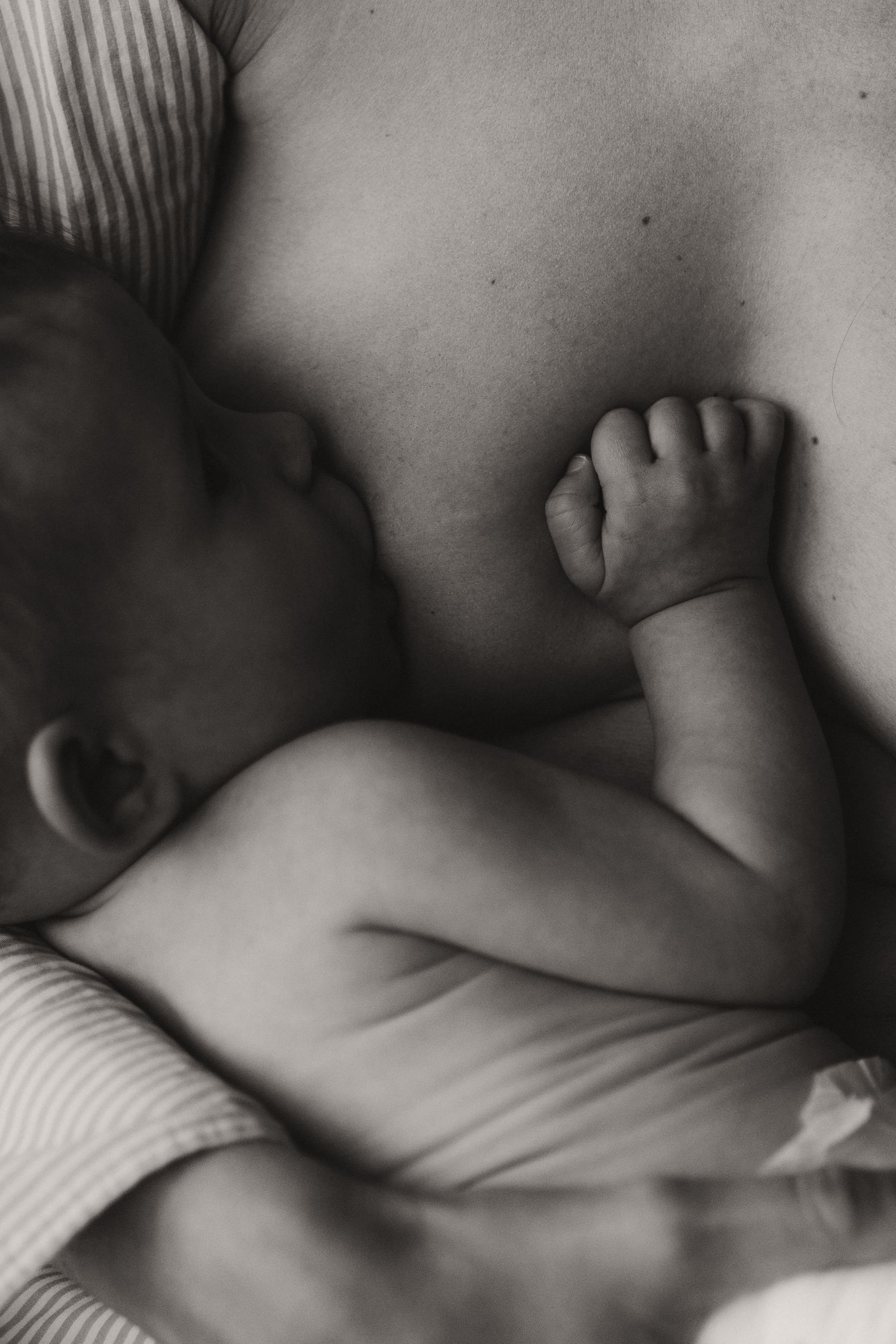Black and white photo of a newborn baby breastfeeding, tiny hand resting on mother's chest.