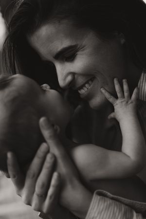 Black and white photo of a smiling mother lovingly holding her newborn baby close to her face.