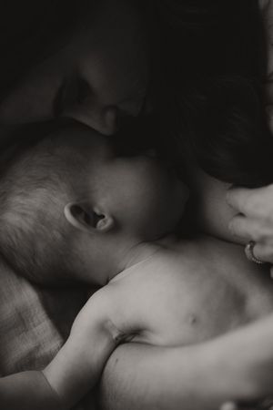 Black and white photo of a mother tenderly kissing her newborn baby, capturing an intimate bonding moment.