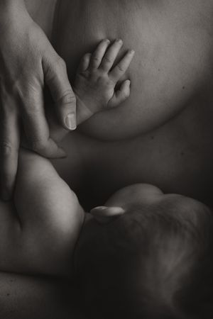 Black and white photo of a newborn baby breastfeeding, tiny hand resting on mothers breast.