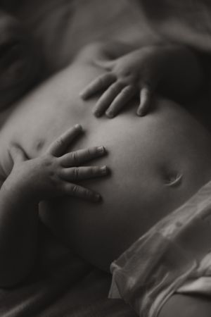Black and white photo of small baby hands resting gently on a pregnant belly.