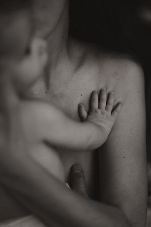 Black and white photo of a newborn baby's tiny hand resting gently on a mother's chest.
