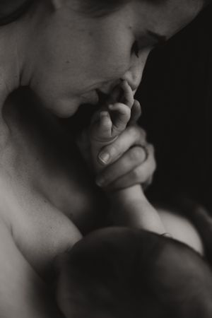 Black and white close-up of a mother tenderly kissing her newborn baby's tiny fingers.