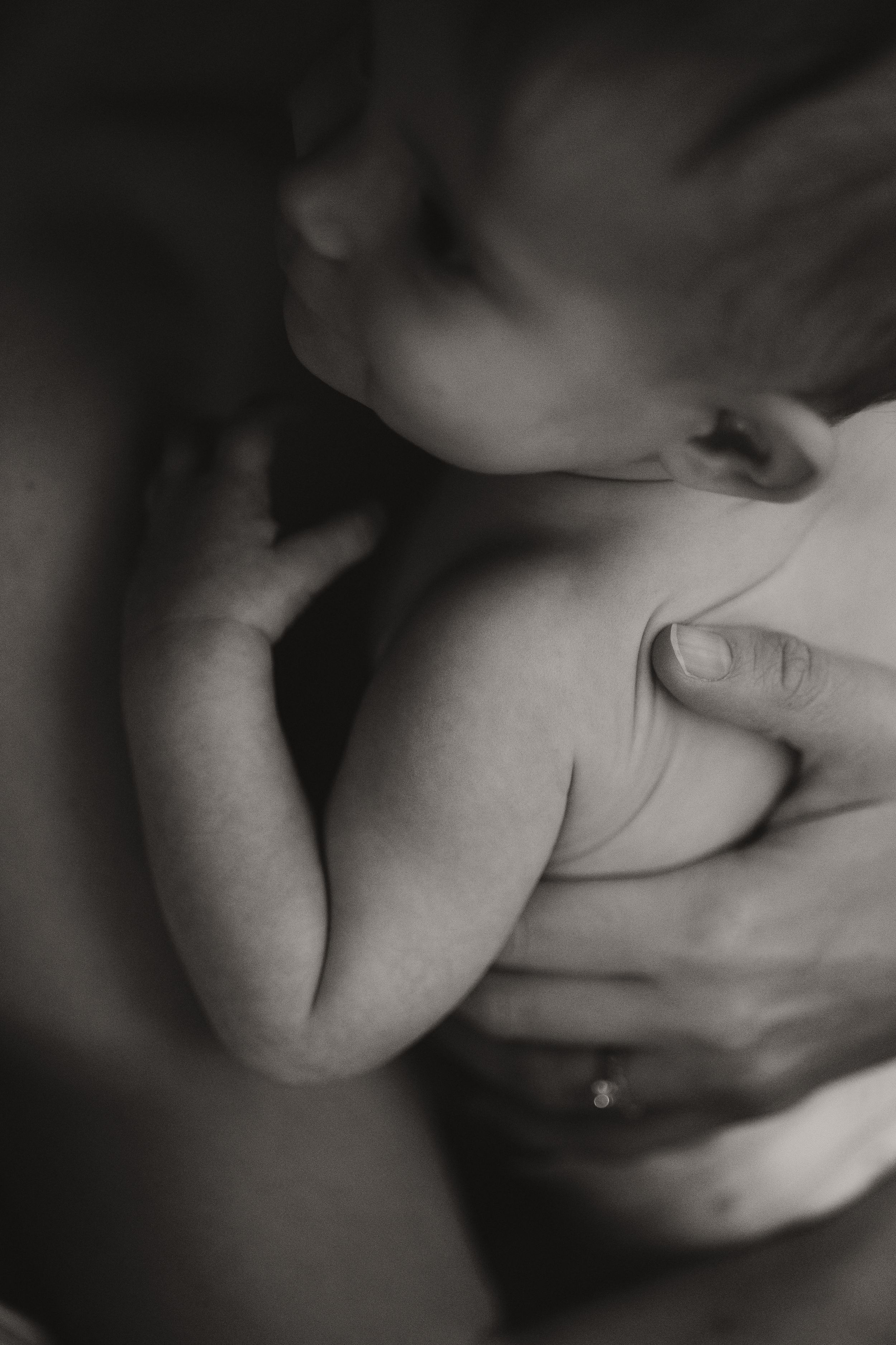 Black and white close-up of a newborn baby being cradled in mother's hands, ring visible on finger.