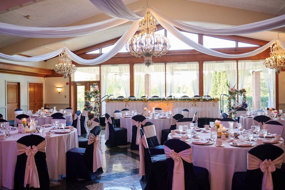 Elegant wedding reception hall with pink and black chair covers, crystal chandeliers, and draped white fabric ceiling decor.