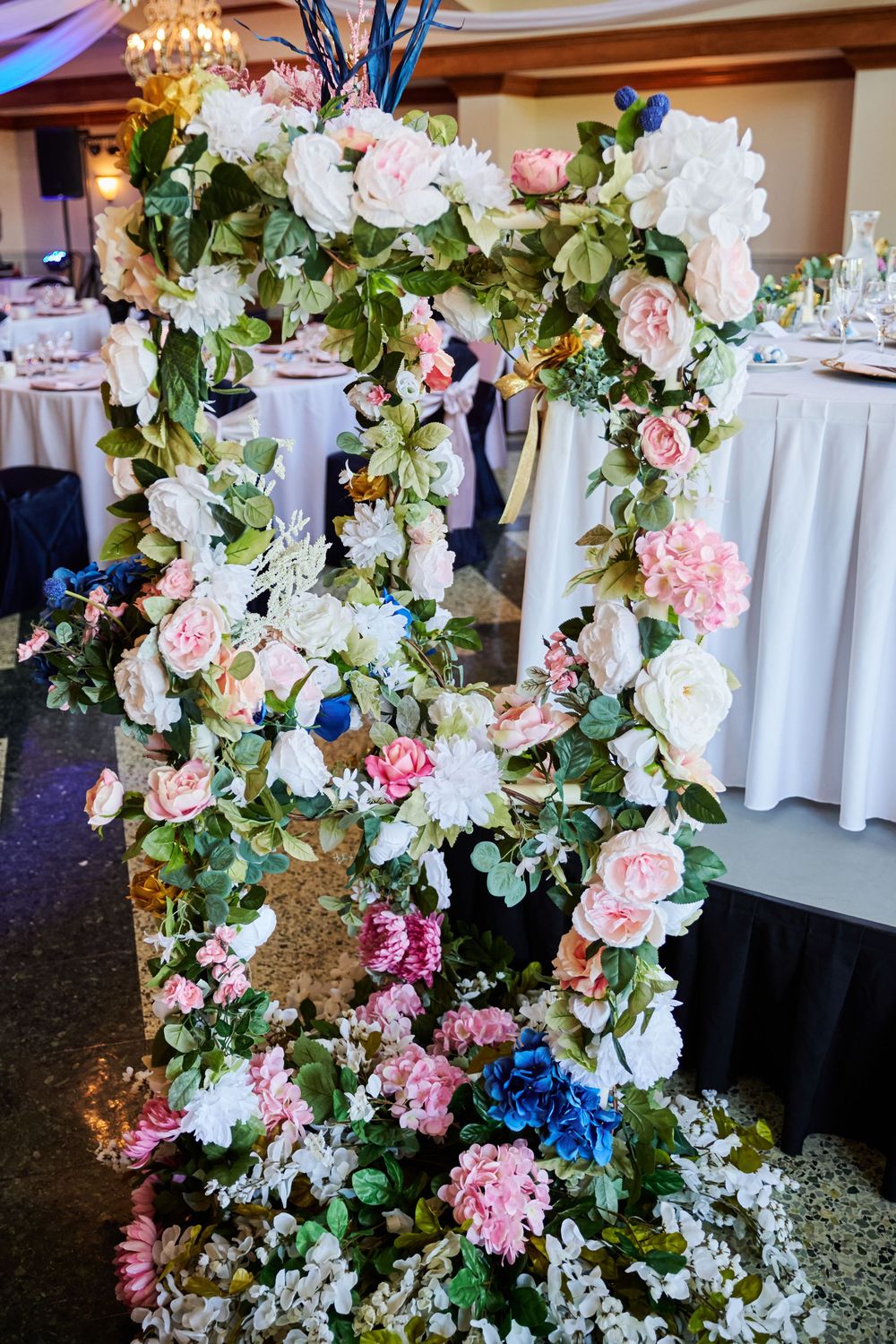 Elegant floral display with pink, white, and blue flowers arranged on a decorative stand in a wedding reception hall.