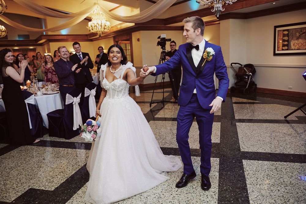 Bride in white gown and groom in blue suit share first dance at elegant wedding reception venue.