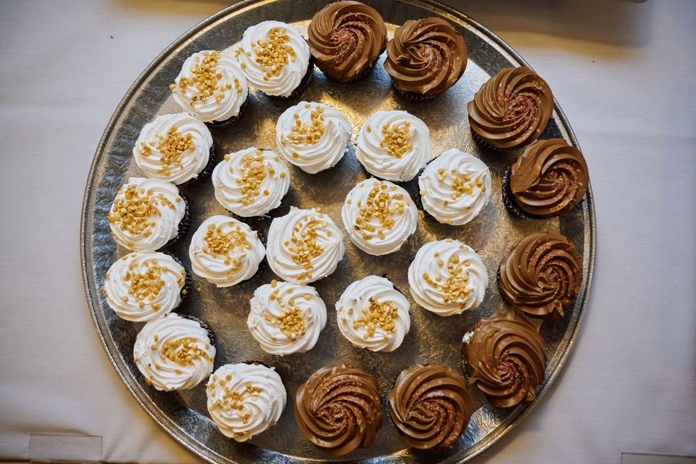 Elegant silver platter displaying assorted cupcakes with white frosting and gold sprinkles alongside chocolate swirl cupcakes.