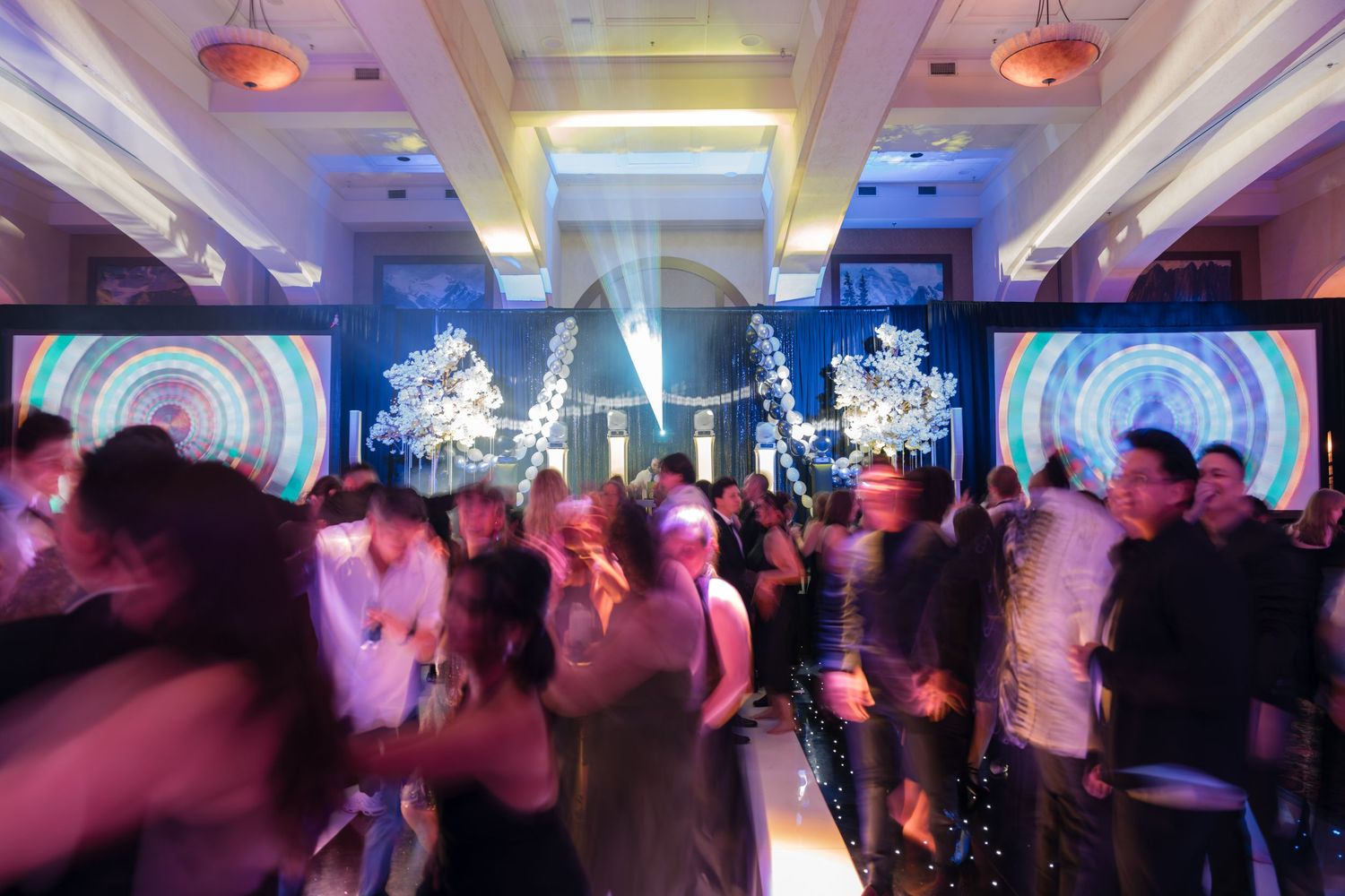 Guests dancing at an elegant event at the Fairmont Chateau Lake Louise with colorful displays and white floral arrangements in a ballroom.