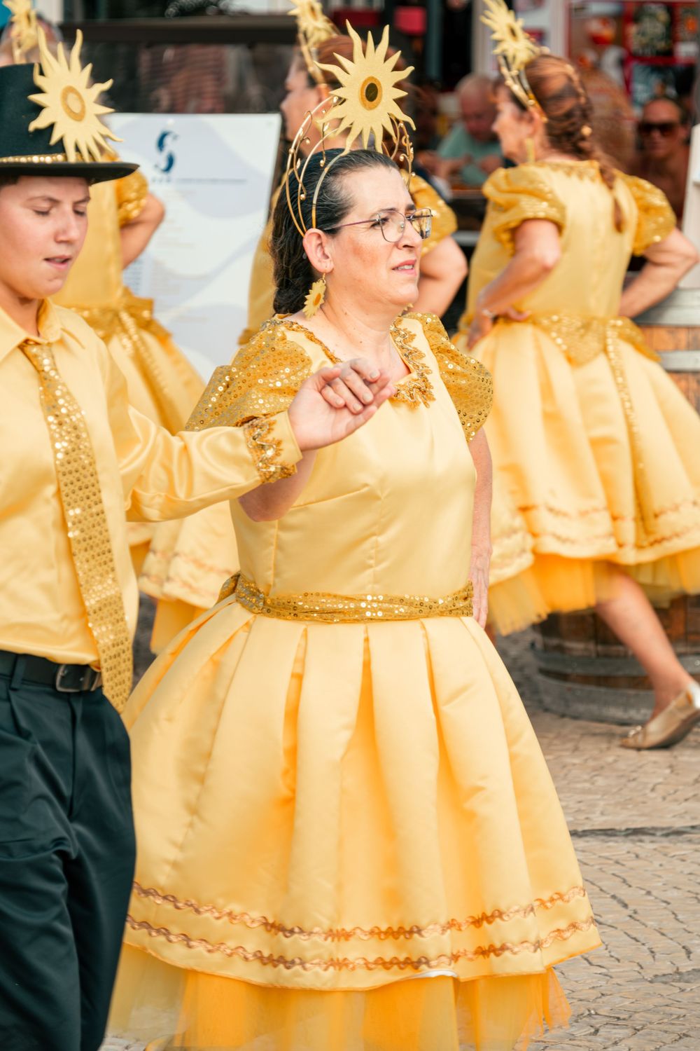 Woman in yellow dress and sun crown dancing at a colorful carnival parade festival celebration.