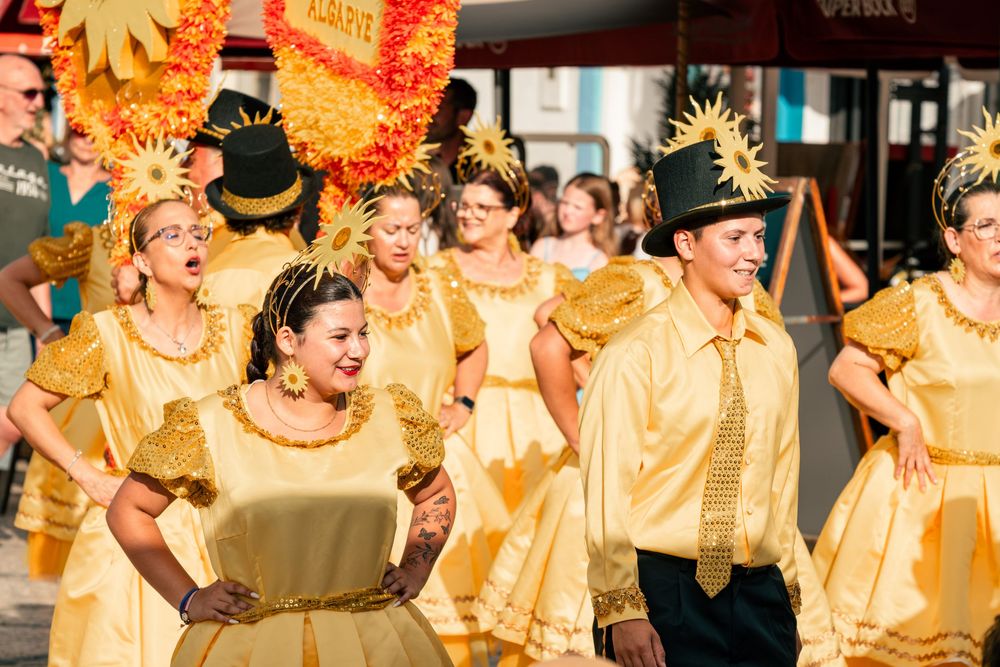 Colorful carnival parade with dancers in golden yellow costumes and black top hats performing in a festive street celebration.