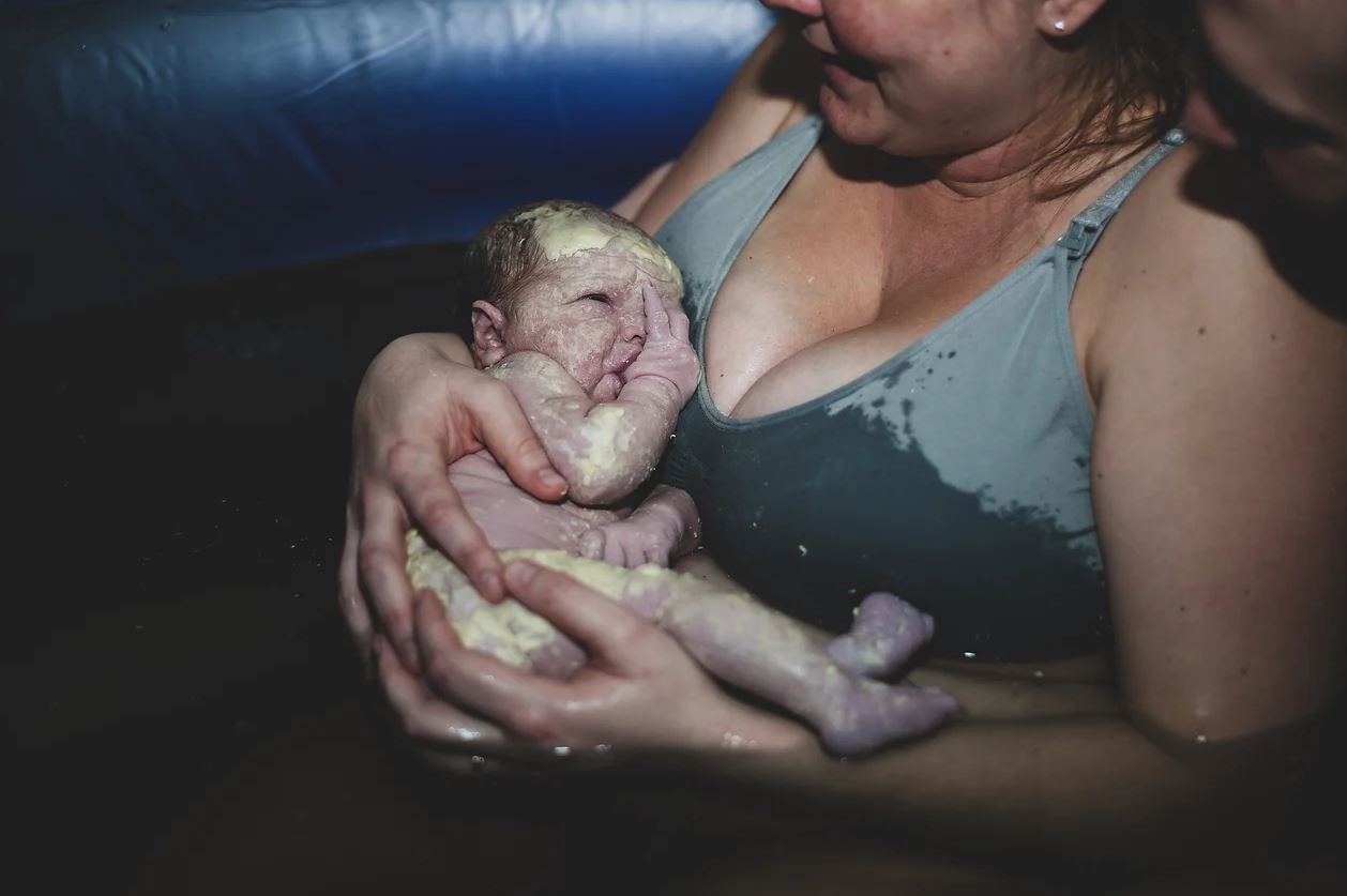 Newborn baby being washed and held during a water birth in a dark setting.