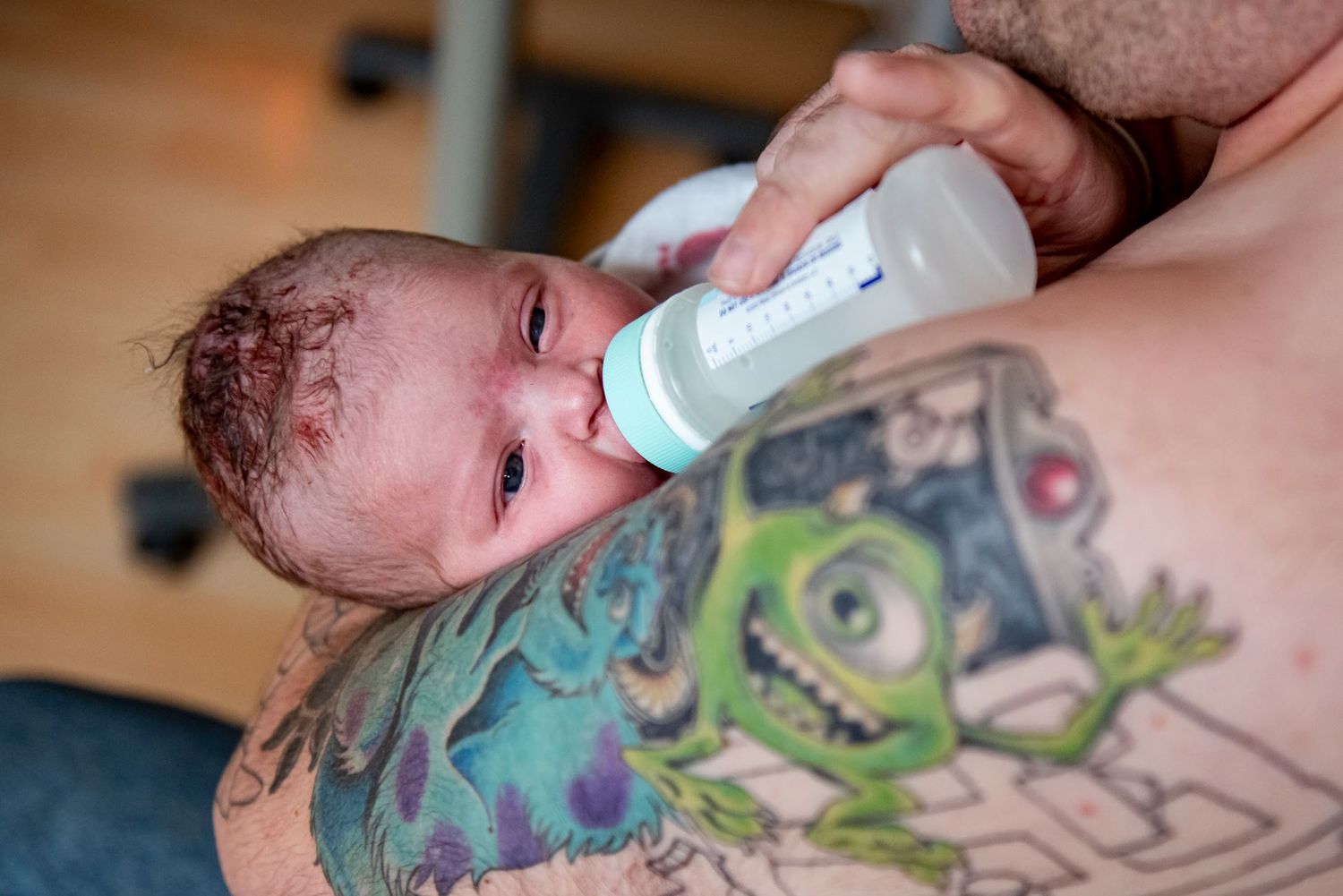 A crying newborn baby being bottle fed shows visible emotion during feeding time.