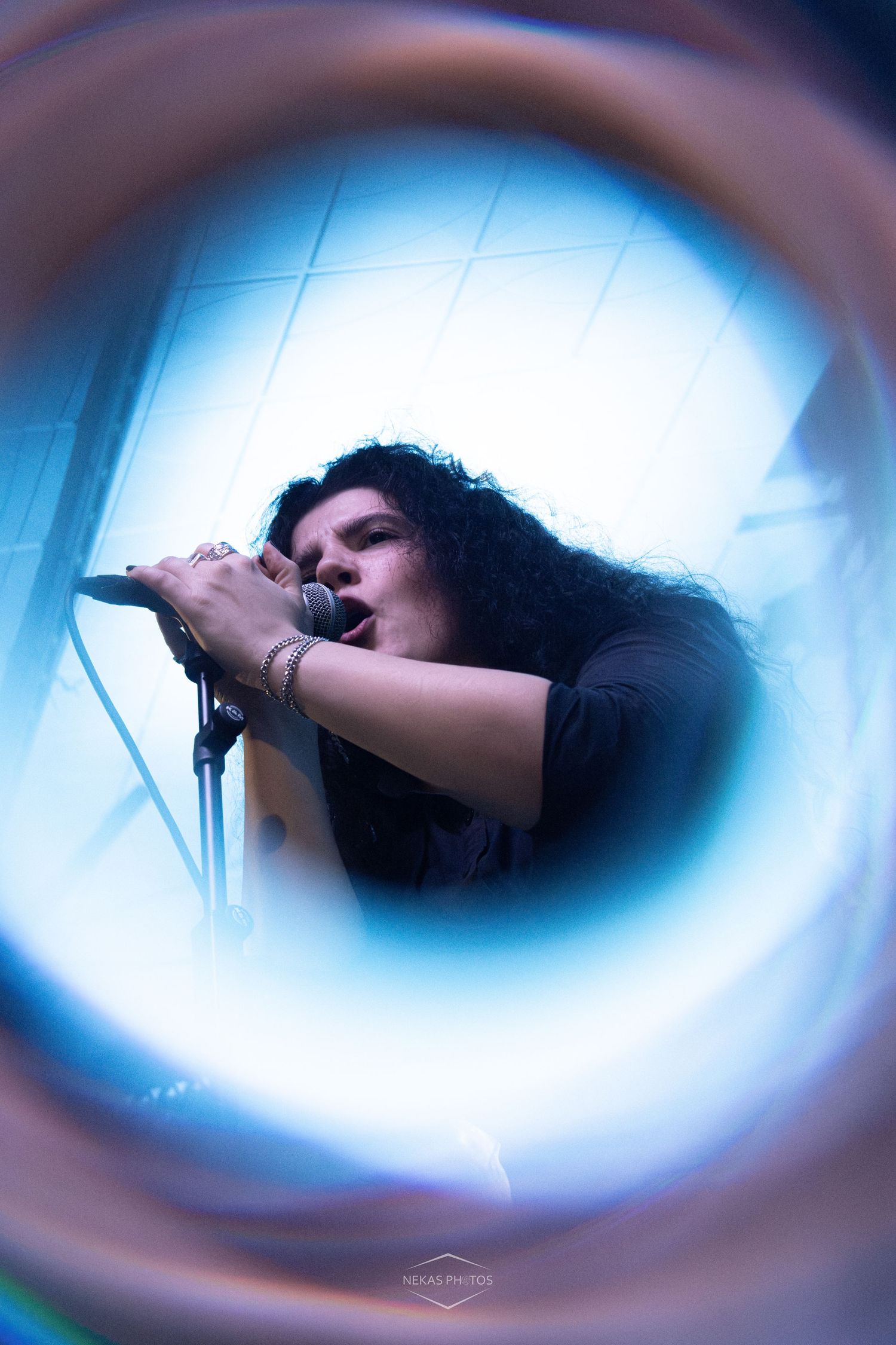 Singer performing live on stage, captured through a circular lens effect with blue lighting.