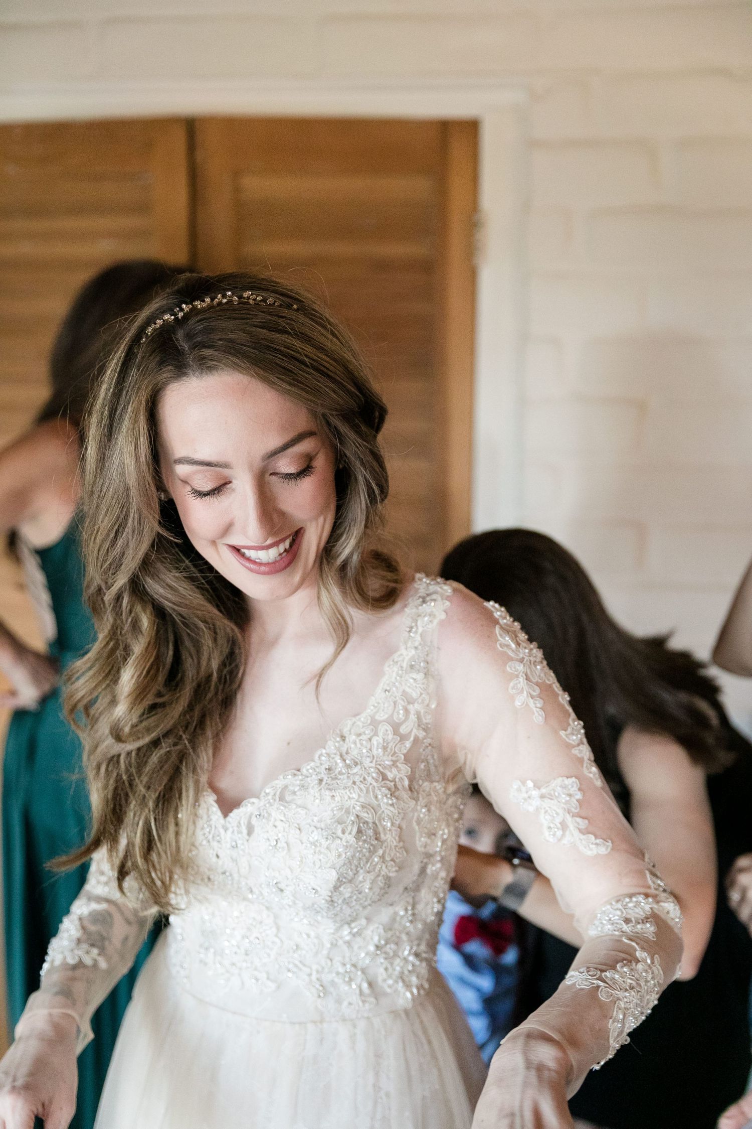 Smiling bride in a lace long-sleeve wedding gown with a delicate crown headpiece getting ready.