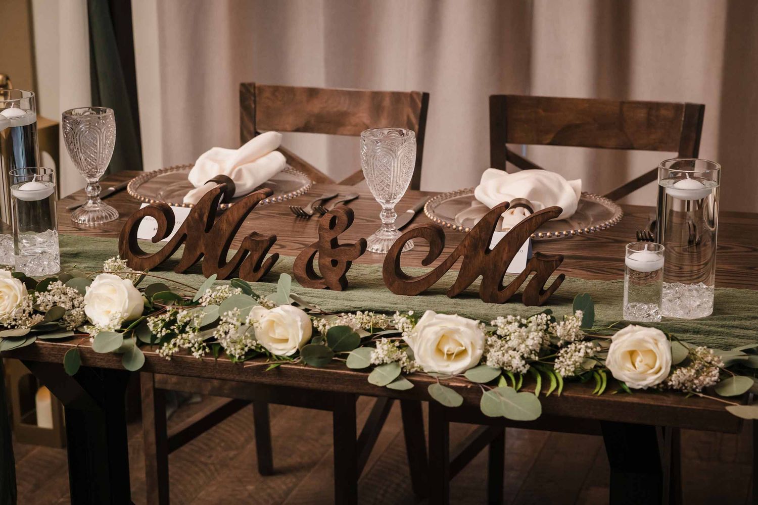 Rustic sweetheart table with greenery garland, white roses, and “Mr & Mrs” wood sign at Briar Barn Inn wedding