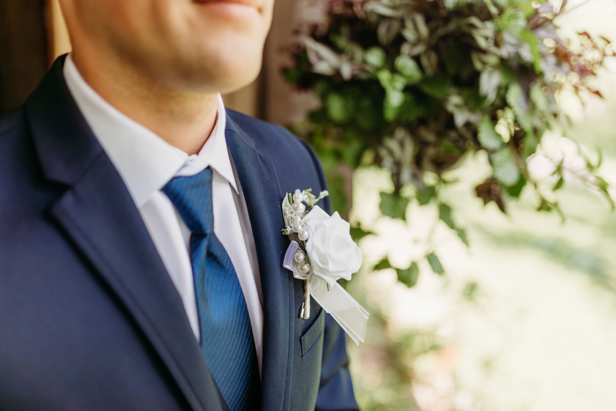 Groom in navy blue suit with white boutonniere and blue tie at wedding ceremony.