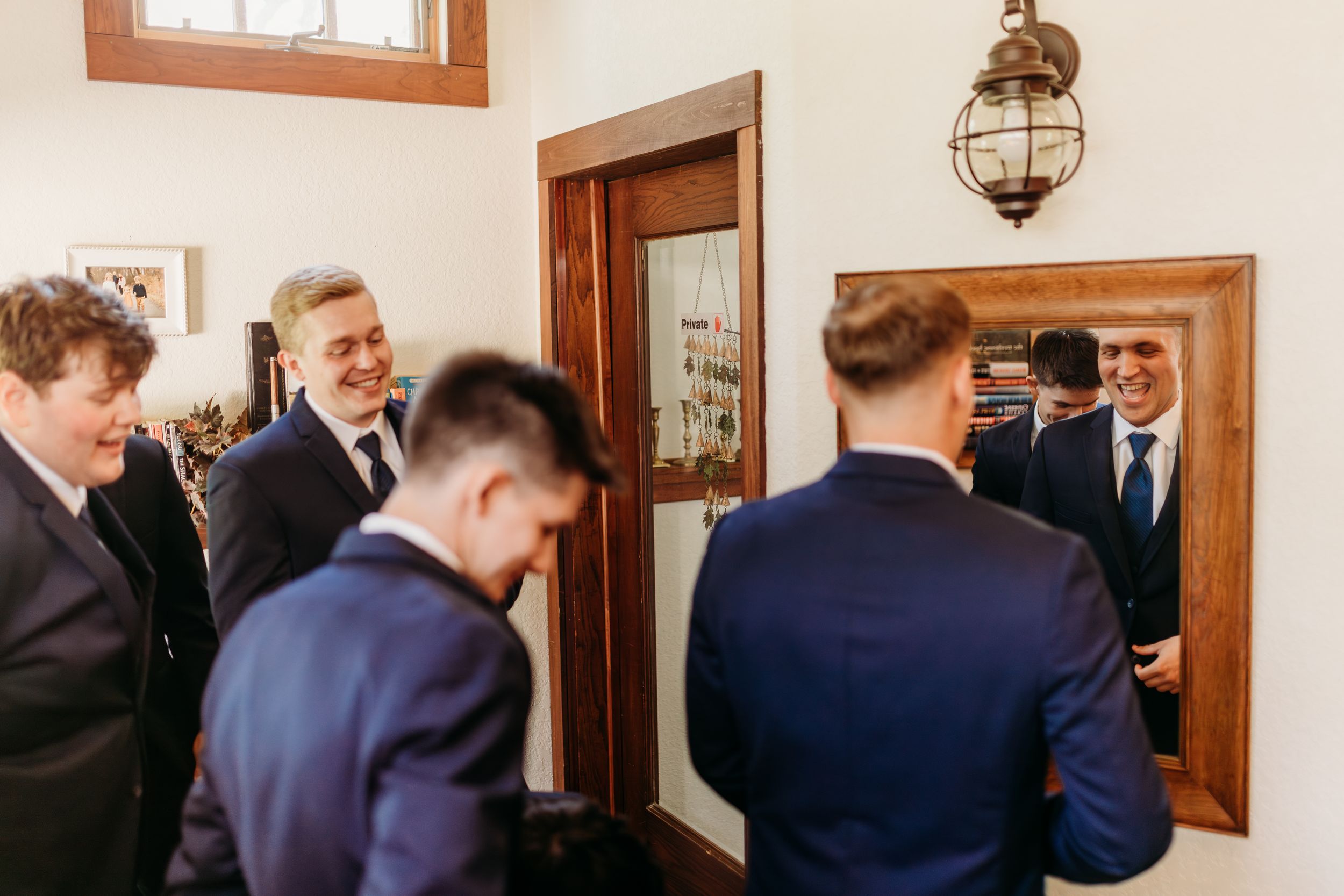 Group of groomsmen in navy suits laughing and chatting while getting ready before wedding.