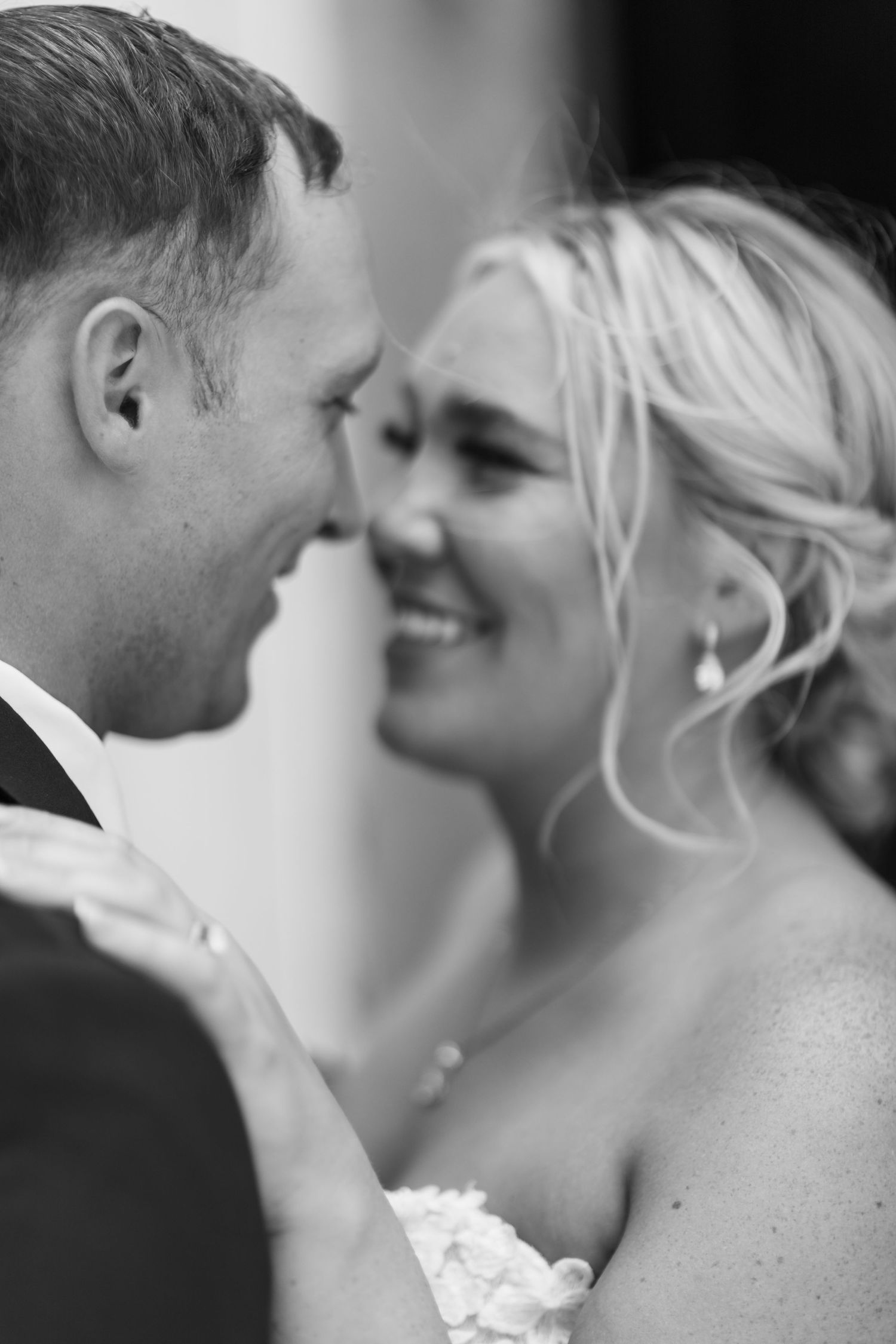 Black and white photo of bride in lace mermaid gown with train embracing groom in dark suit at wedding.