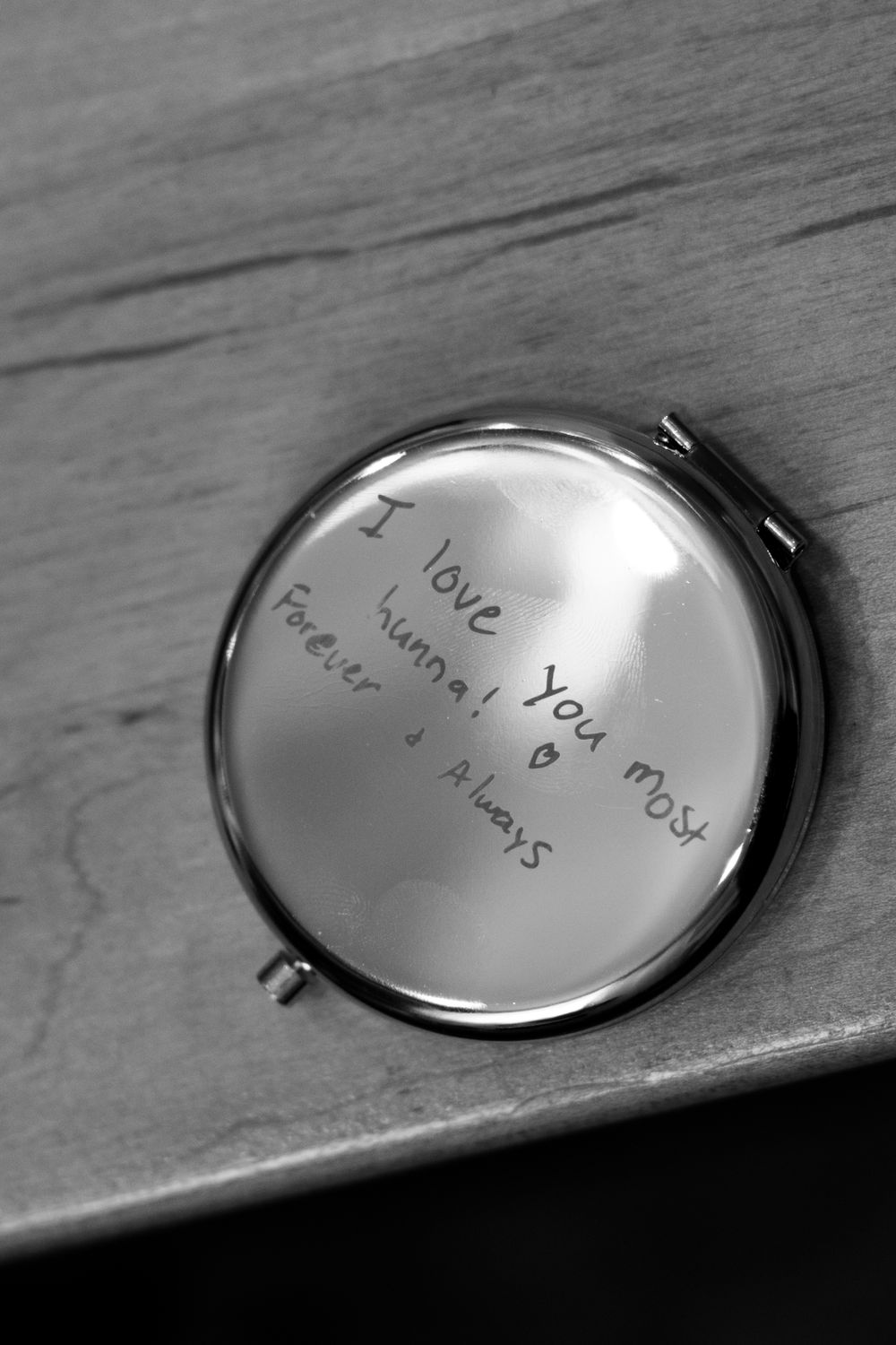 Black and white photo of a compact mirror engraved with handwritten message I love you most, hanna, forever and always.