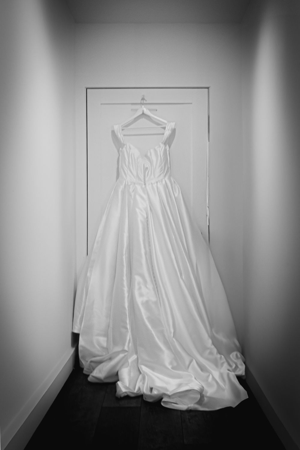 Elegant white wedding ball gown with sweetheart neckline hanging on a door in black and white photo.