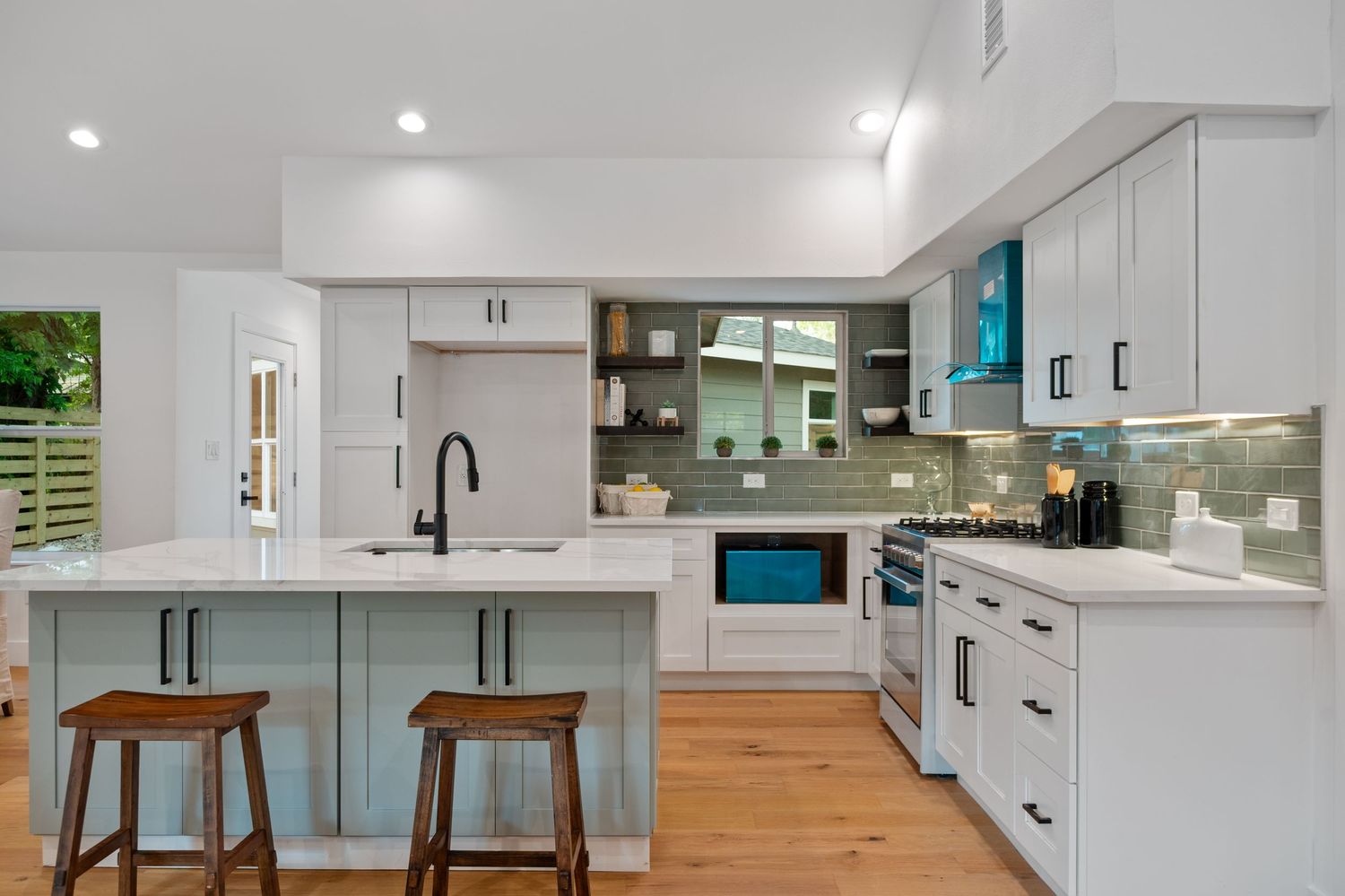 Contemporary kitchen featuring white cabinets, wood barstools, and teal accents with modern fixtures.