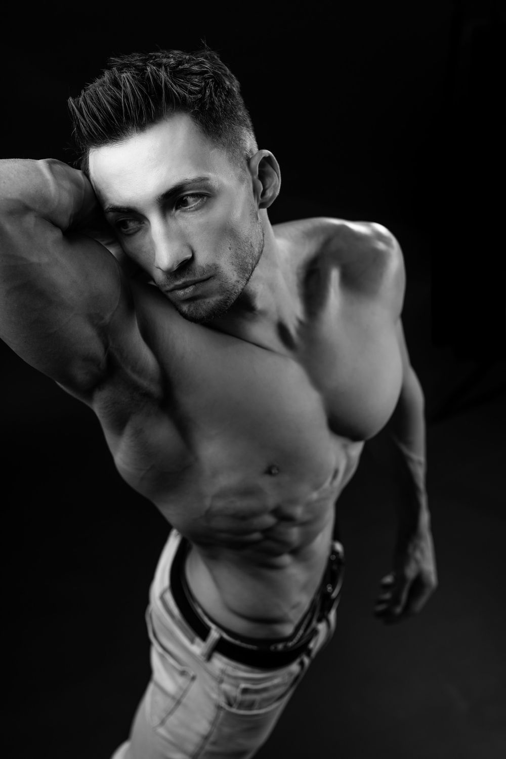 Black and white photo of a muscular shirtless man posing confidently against a dark background.