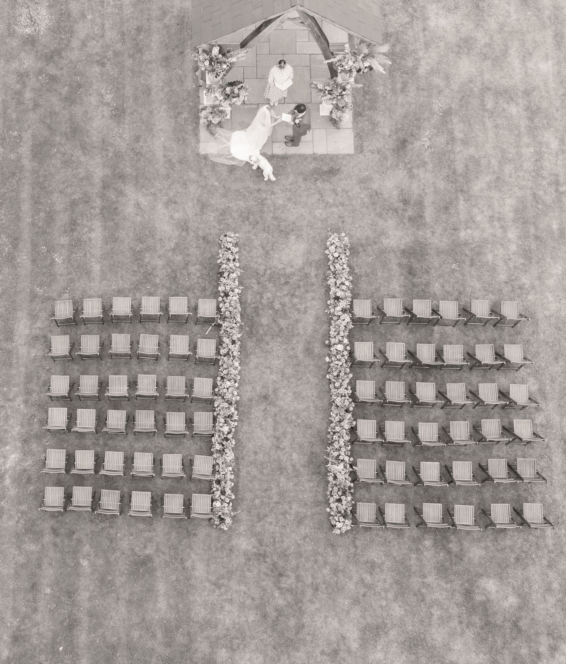 Aerial view of wedding ceremony chairs arranged in two sections with floral aisle decor and a nativity sign above.