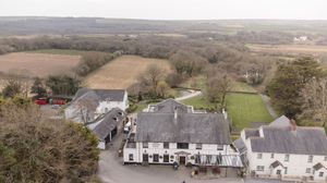 Aerial view of a rural countryside inn surrounded by green fields and trees in a scenic landscape.