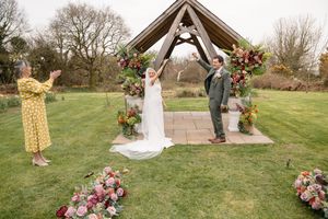 Bride and groom celebrate under a wooden arch adorned with flowers at an outdoor garden wedding ceremony.
