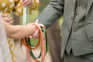 Couple's hands bound together with colorful ribbons during a wedding handfasting ceremony.