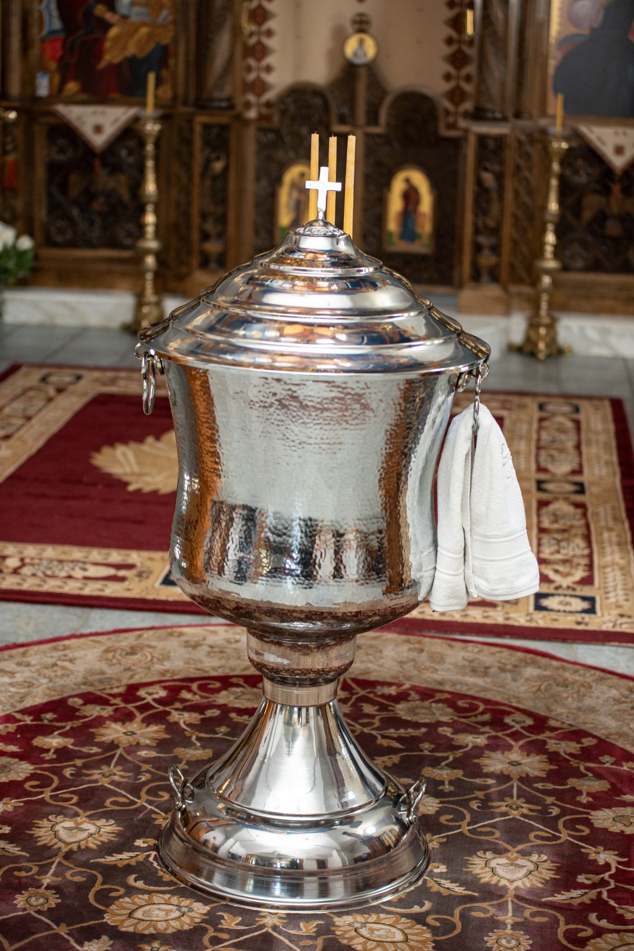 A ornate silver baptismal font with a cross on top inside an Orthodox Christian church.
