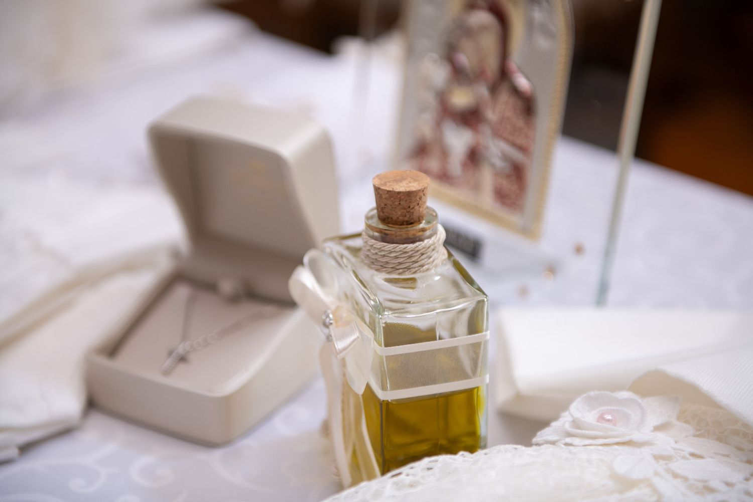 A bottle of holy anointing oil with a cross necklace and religious icon for an Orthodox baptism.