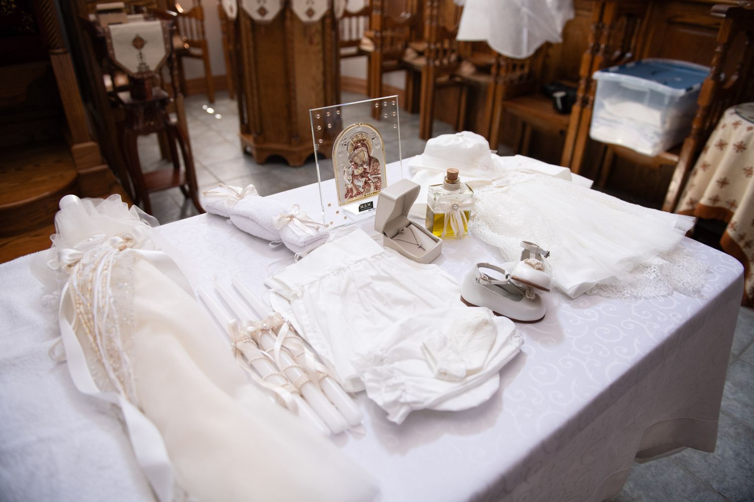 Baptism accessories including white garments, holy oil, and a religious icon arranged on a white table.