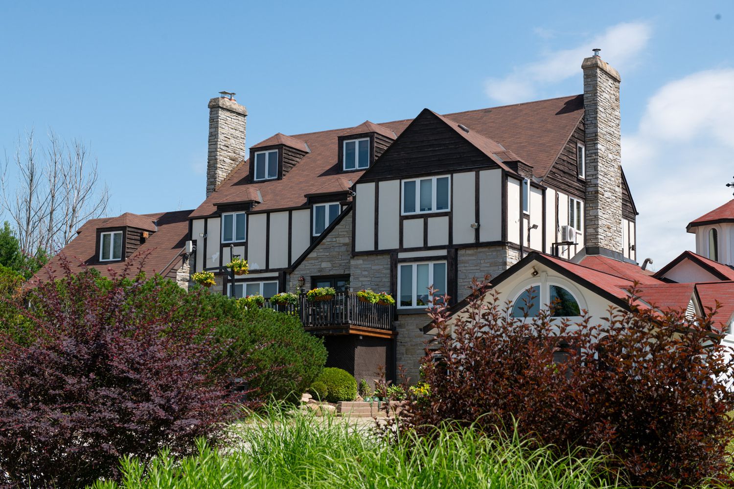 A large Tudor-style house with chimneys surrounded by lush green trees and shrubs.
