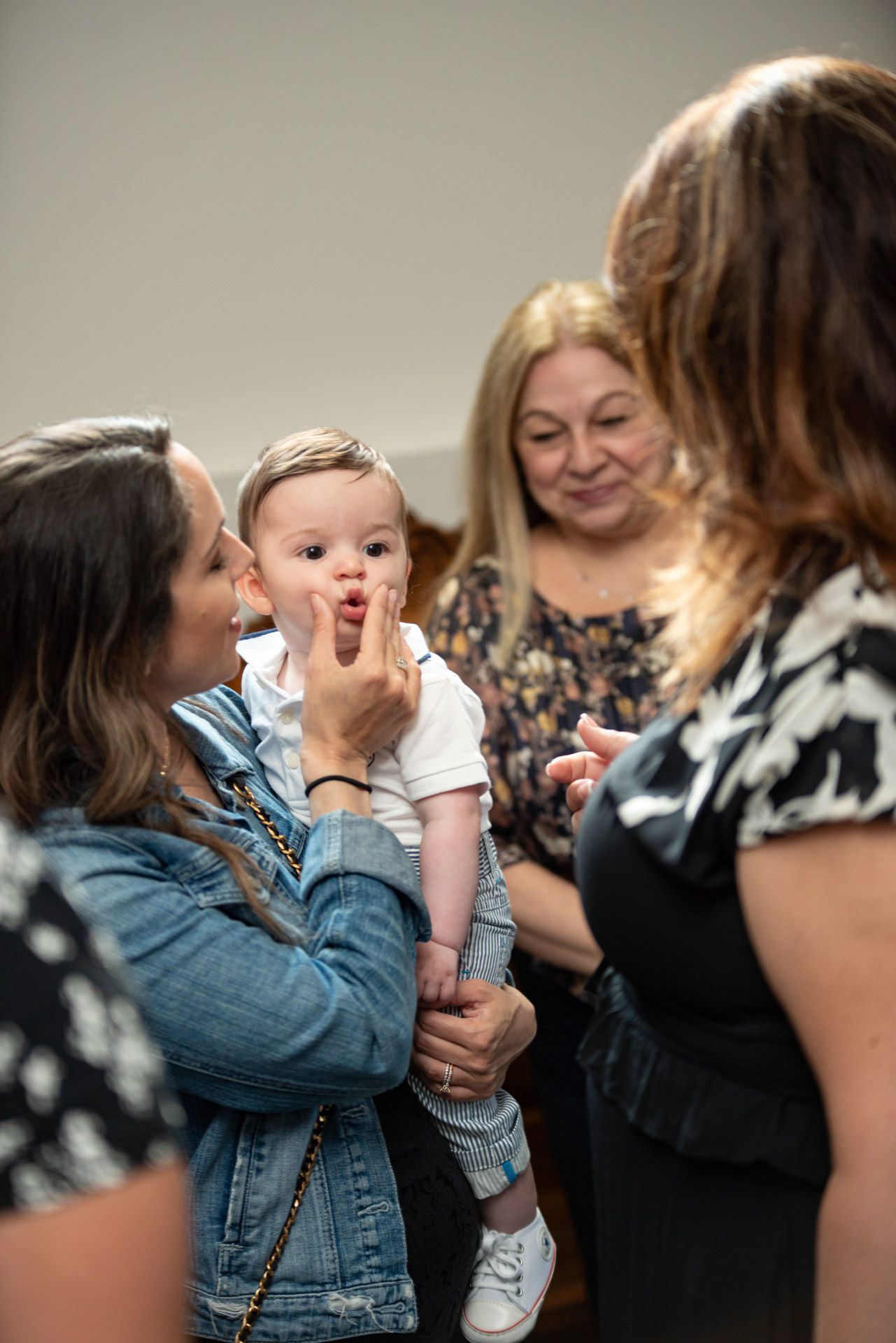 Woman holding baby at christening reception while guests admire the infant.