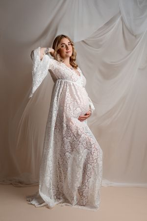 A maternity photoshoot featuring a flowing white lace dress against a light backdrop with elegant poses.