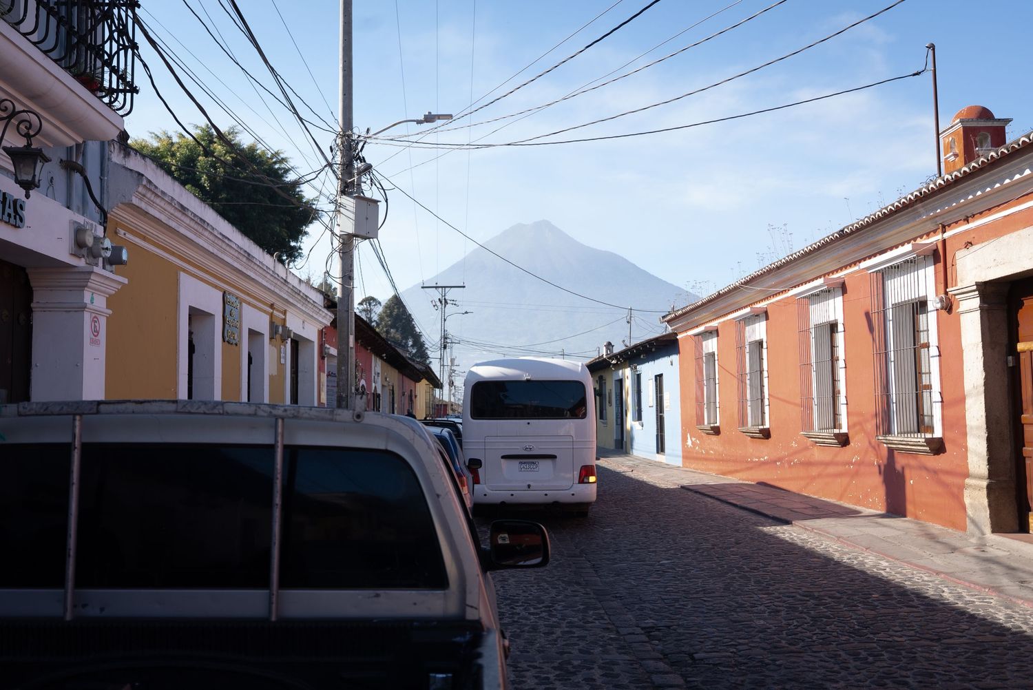 A row of colorful colonial buildings line a cobblestone street in Trinidad, Cuba with power lines overhead.