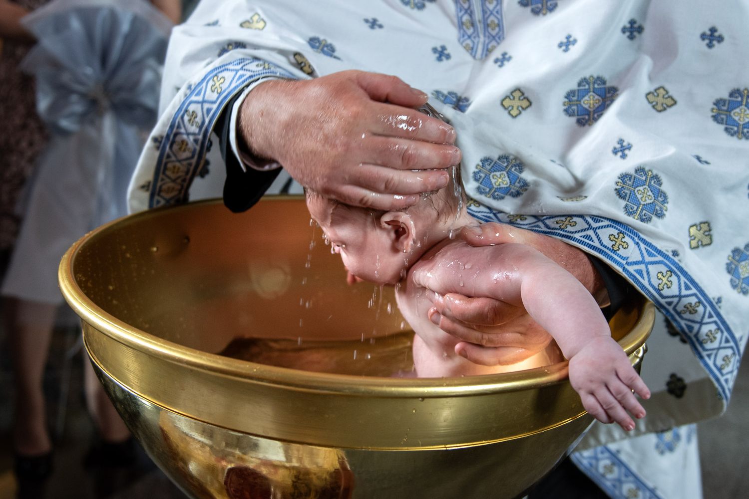 Orthodox priest baptizes infant in golden font during religious ceremony.