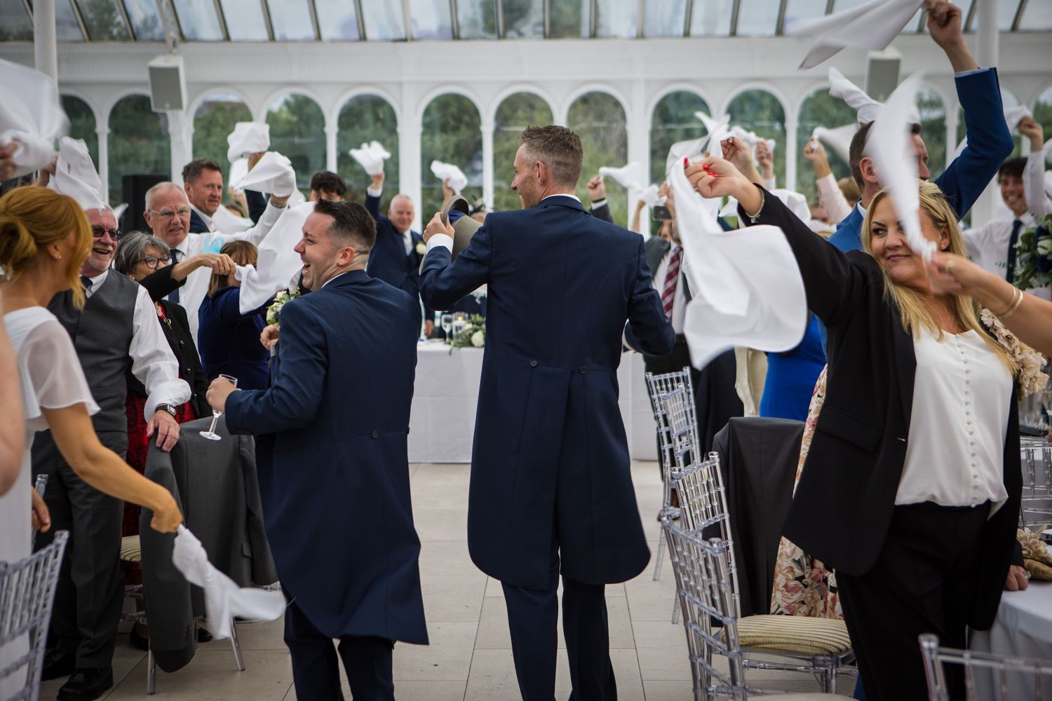 Wedding celebration in elegant conservatory venue with white columns and glass ceiling.