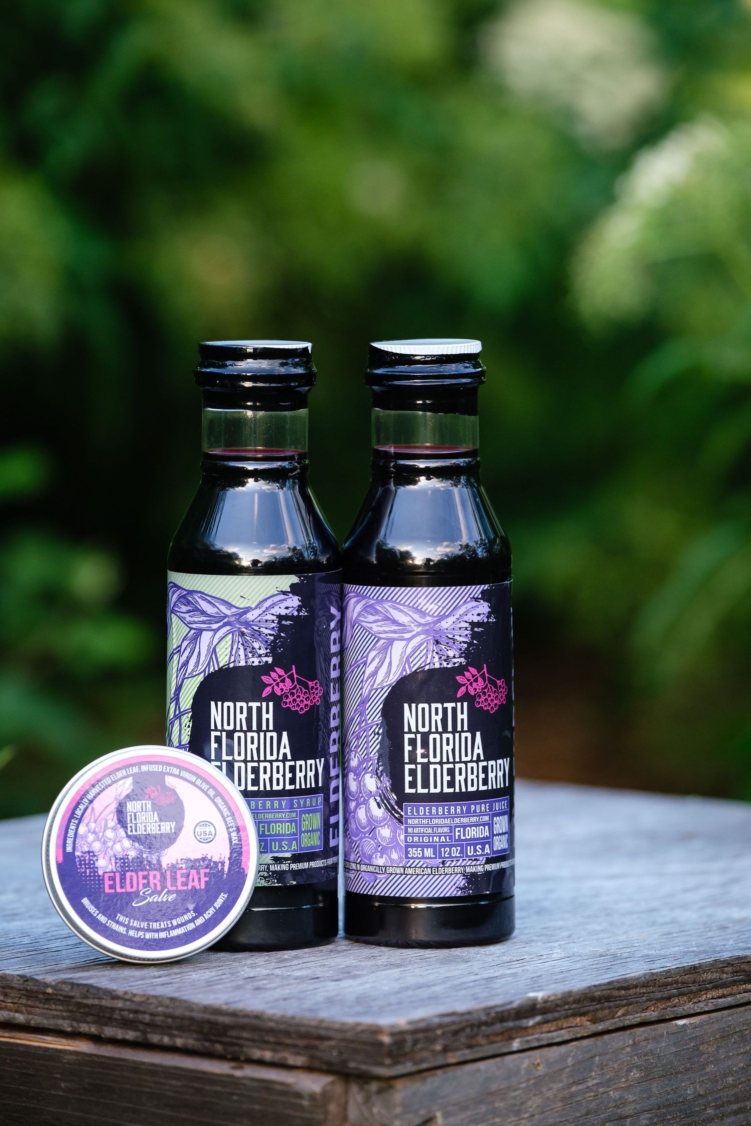 Two bottle of elderberry juice and a can of elderberry cream sit on a rustic wooden box.