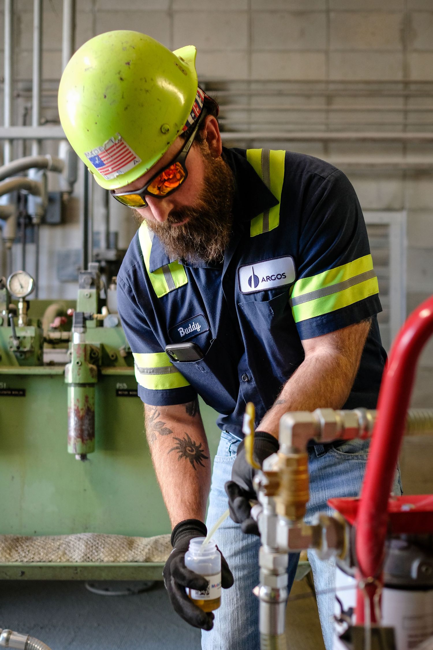 An environmental portrait of a man wearing a yellow hard hat and a blue work shirt with yellow stripes and safety glasses.