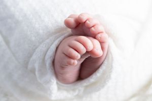Close-up of a newborn baby's tiny feet and hands wrapped in a soft white blanket.