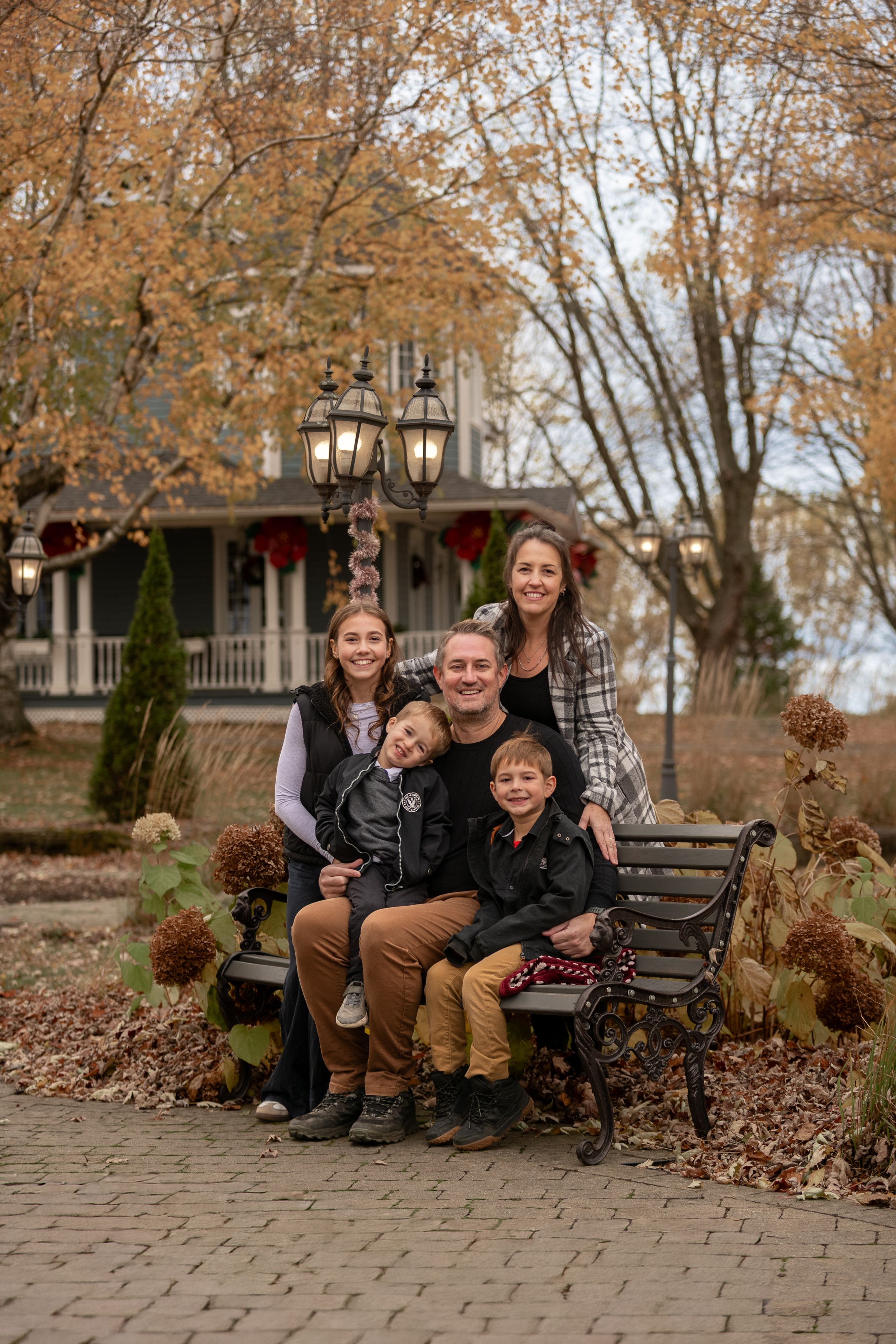 A group sits together on a park bench surrounded by fall foliage and a vintage lamp post on a brick pathway.