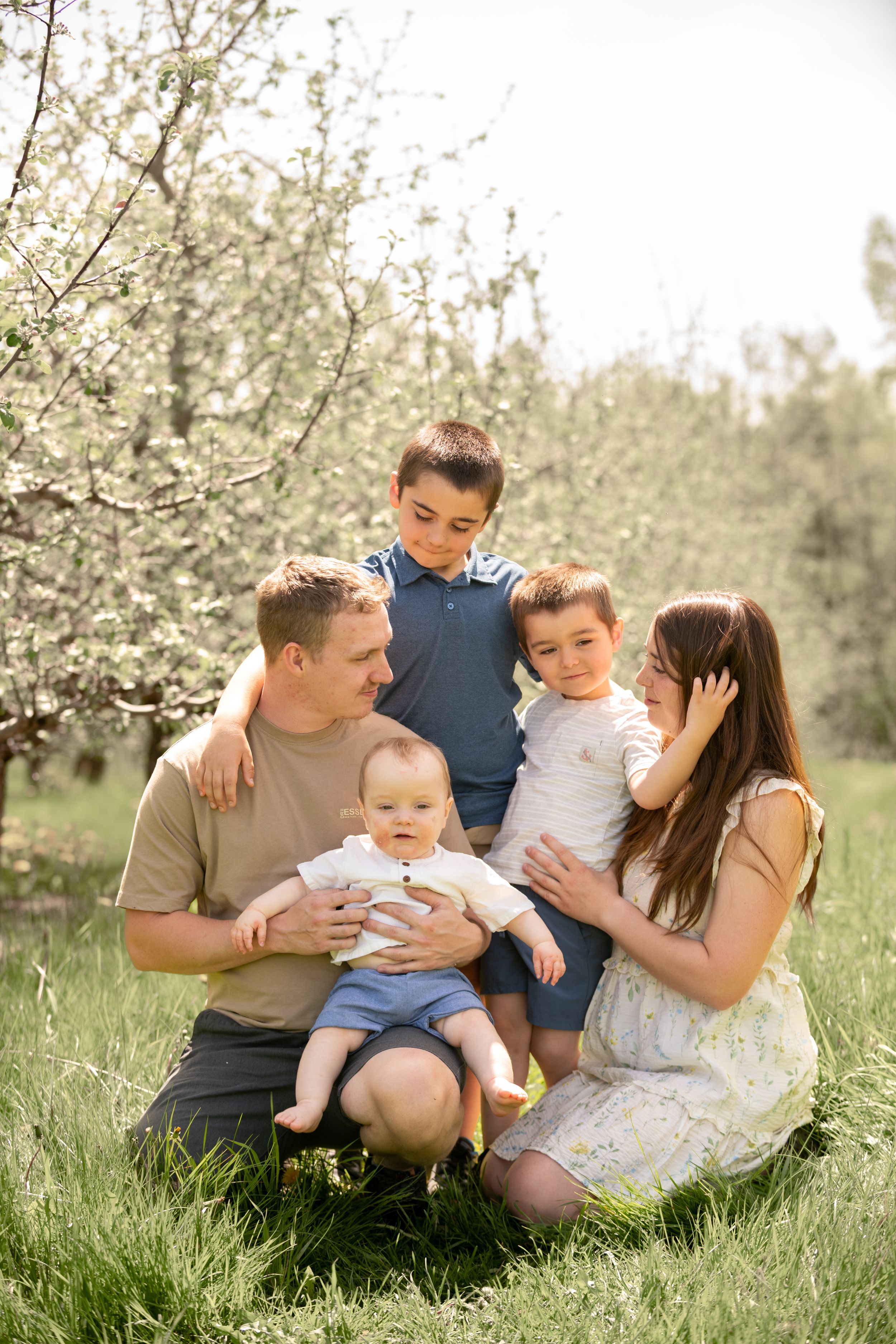 Happy family with three children sitting on grass near blooming trees in a sunny spring garden.